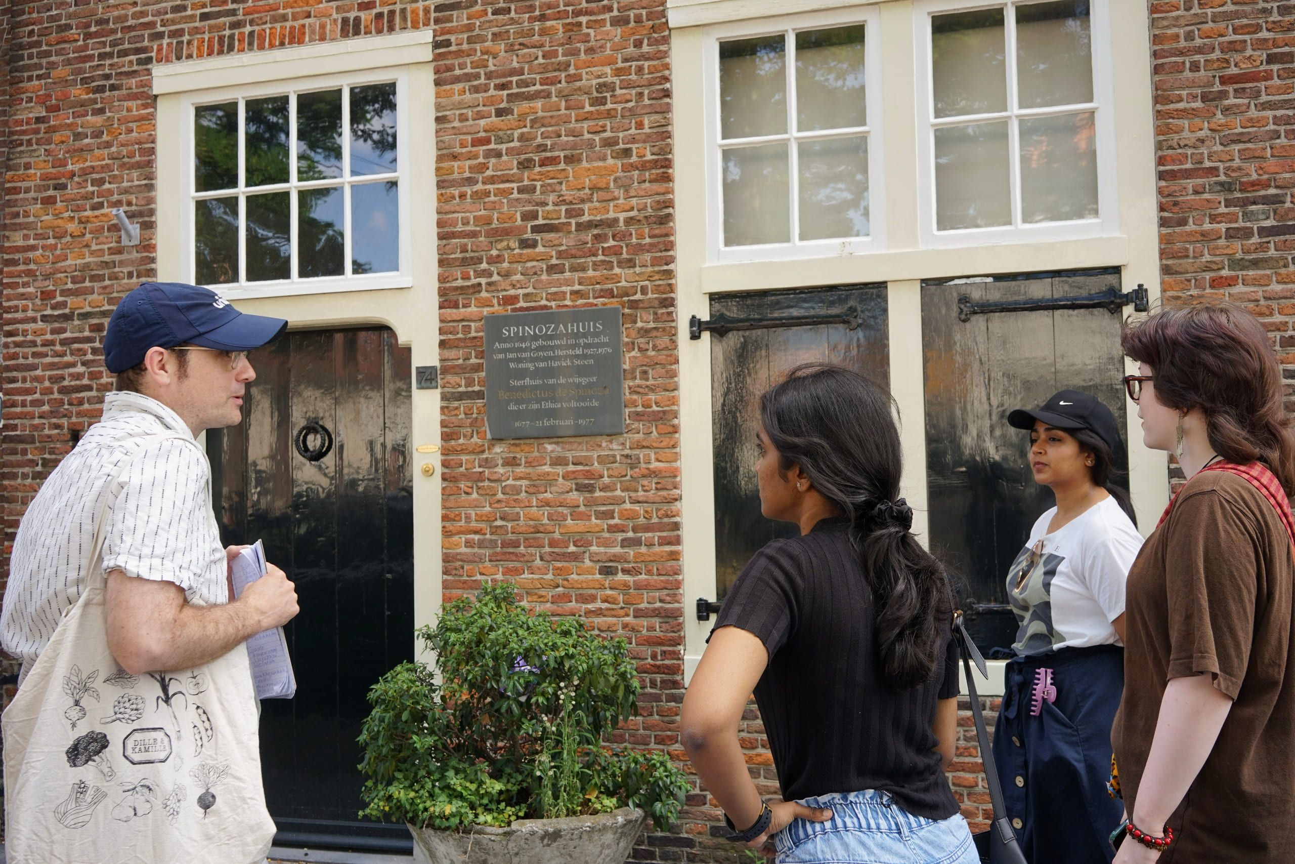 A guide points out a heritage plaque on a canal-house facade in Den Haag while a small group looks on.