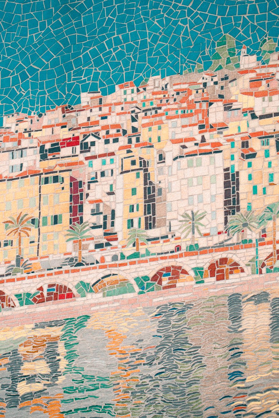 A tiled mosaic of a Riviera old town — pastel houses stacked under terracotta roofs, an arcaded quay and palms, reflected in the harbour water below.